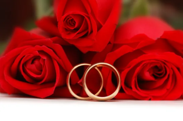 Två guld vigselringar och röda rosor — Stockfoto