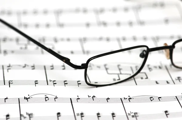 Black reading glasses over the music sheets — Stock Photo, Image