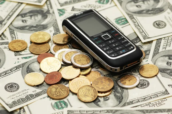 Telefone celular com moedas e notas de dólar — Fotografia de Stock