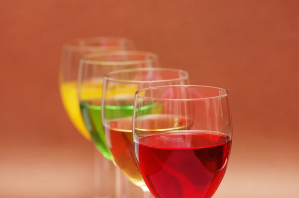 Glazen met dranken van verschillende kleuren op biege achtergrond — Stockfoto