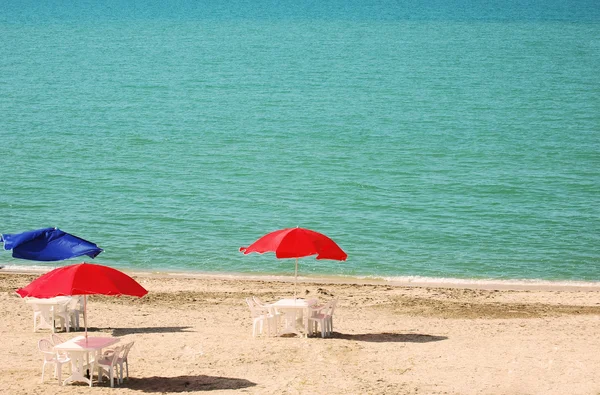 Drei Tische mit Sonnenschirmen am Sommerstrand — Stockfoto
