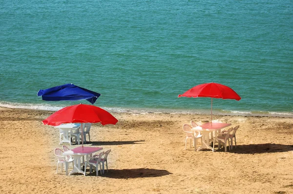 Kolme pöytää päivänvarjoilla kesärannalla — kuvapankkivalokuva
