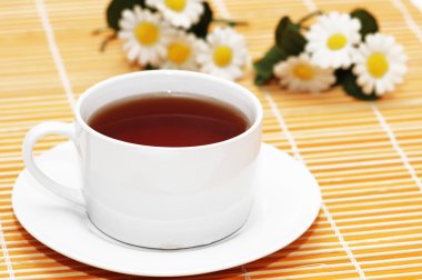 Cup of black tea and camomiles at the background clipart