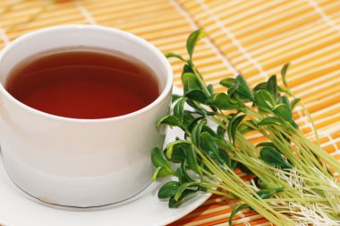 Cup of black tea and herbs on orange mat clipart