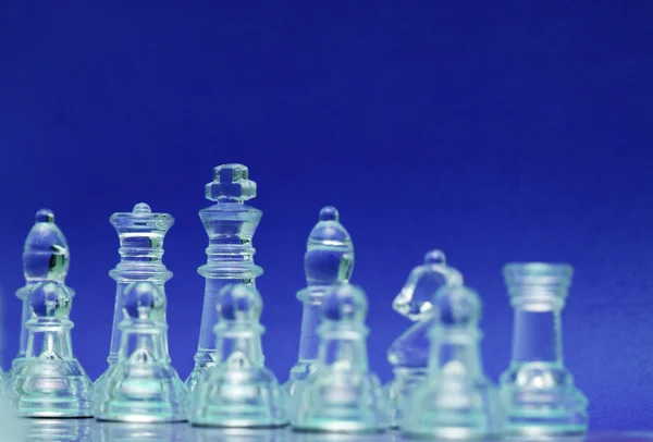 Стеклянные шахматные фигуры на синем фоне — стоковое фото