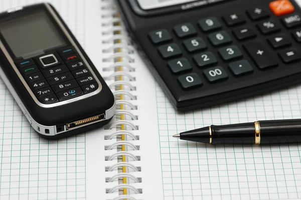 Handy, Taschenrechner und Stift am Notizbuch — Stockfoto