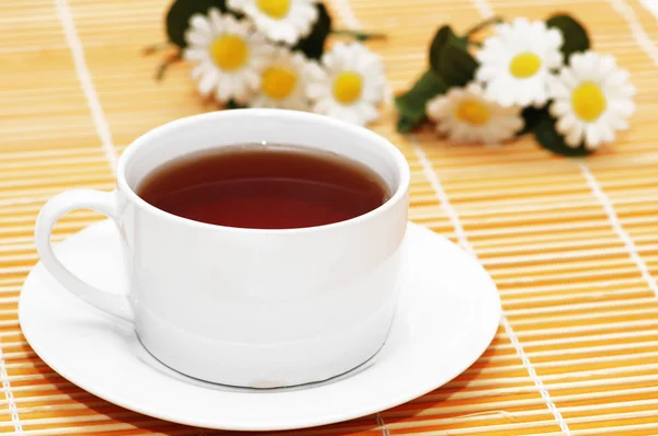 Xícara de chá preto e camomilas no fundo — Fotografia de Stock