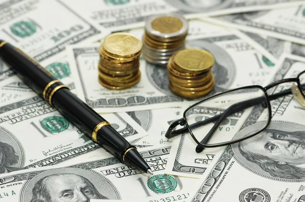 Moedas, caneta e óculos sobre as notas de banco de cem dólares — Fotografia de Stock