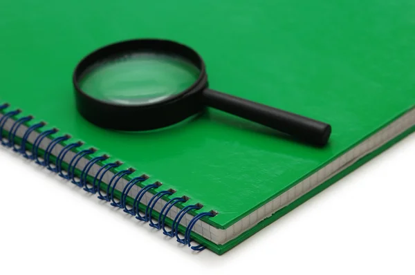 Magnifying glass over the green notebook isolated on white — Stock Photo, Image