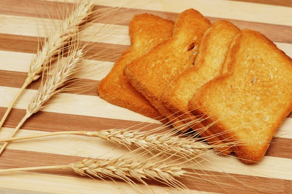 Quattro pezzi tostati e spighe di grano su tavola di legno — Foto Stock