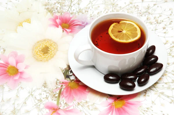 Tea with lemon and chocolates on floral background — Stock Photo, Image