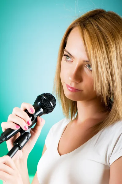 Tjej sjunger med mikrofon mot tonad bakgrund — Stockfoto