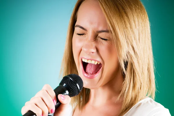 Fille chantant avec microphone sur fond dégradé — Photo