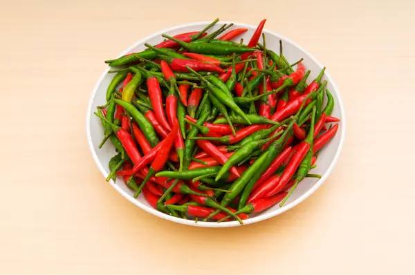 Hot peppers in the plate on wooden table — Stock Photo, Image