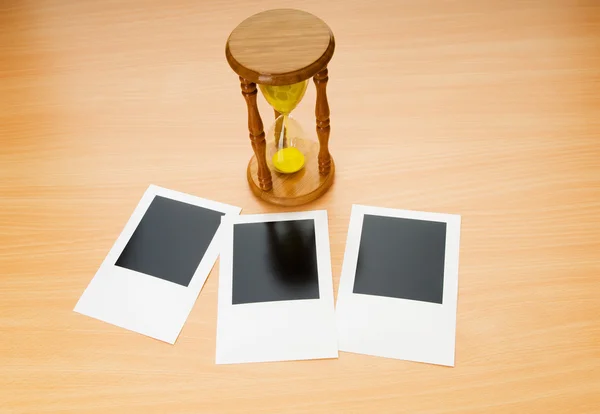 Fotos instantâneas em branco e vidro de hora na mesa de madeira — Fotografia de Stock