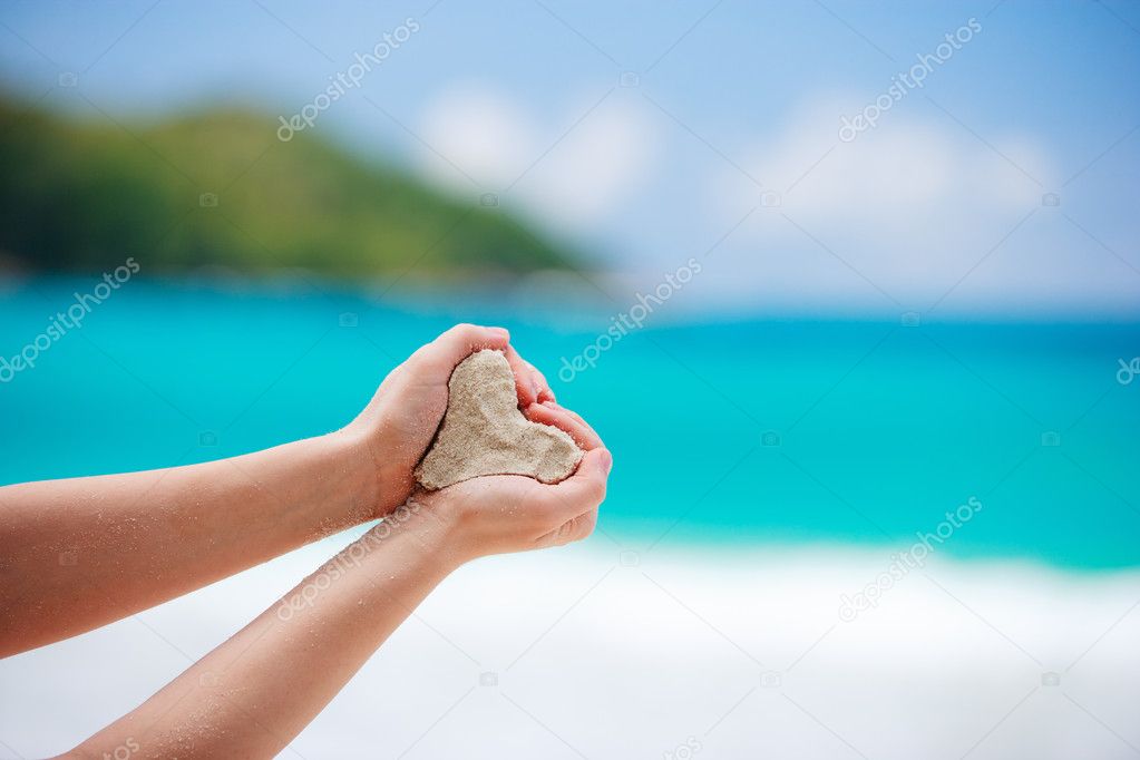 Closeup of woman hands holding white tropical beach form heart shape
