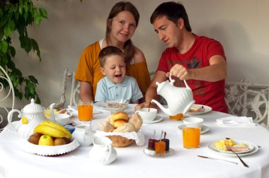 Family of three having breakfast at terrace of theirs house clipart