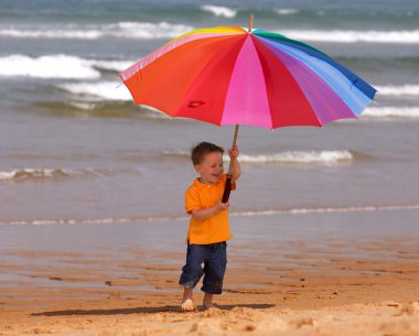 Do not depend on weather conditions. Cute small boy with big brightly colored umbrella having fun on the beach clipart