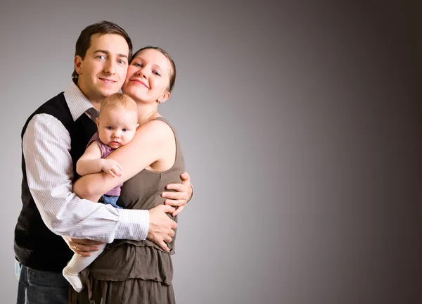 工作室女孩的照片快乐年轻的父母和 个月旧婴儿在黑暗的灰色背景 — 图库照片