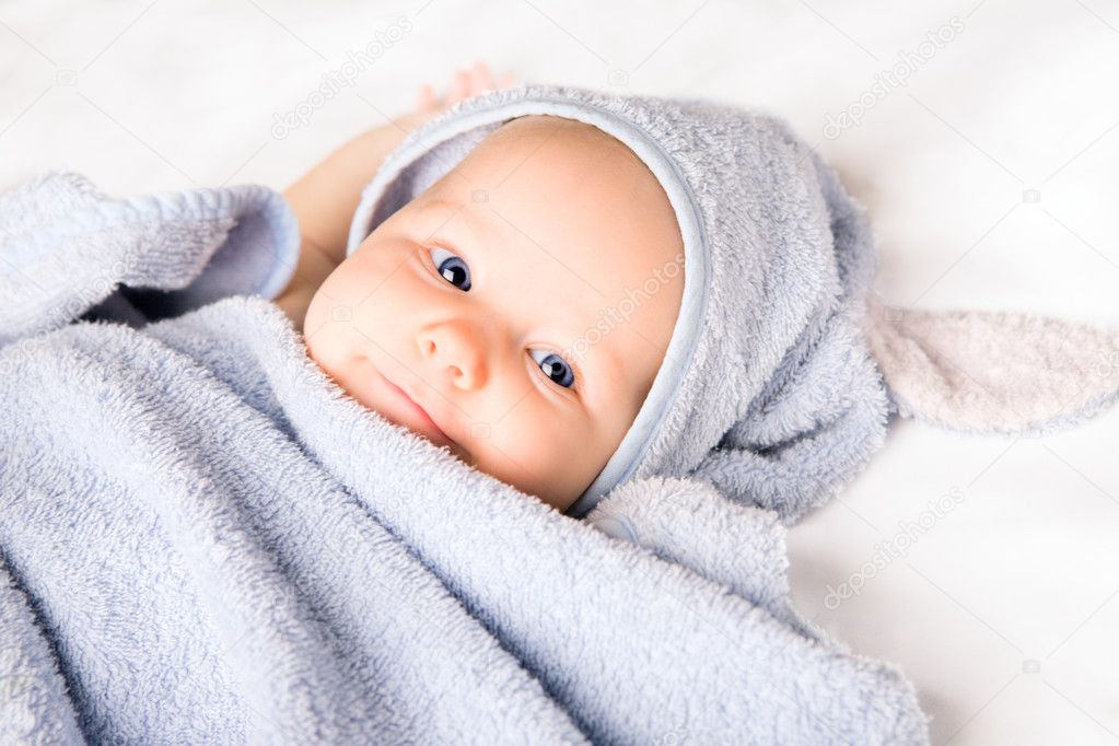 Cute baby girl with towel after bath on white blanket