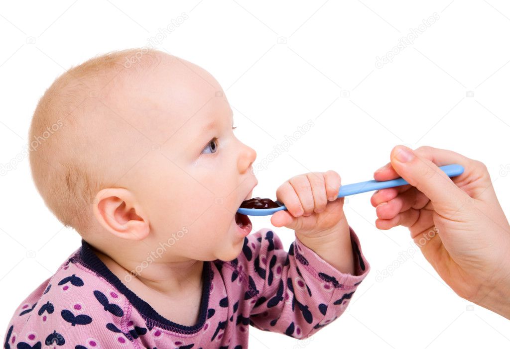 Little girl eating baby food with spoon. Isolated on white