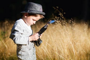 Stylish small boy with retro camera photographing outdoors at sunny autumn day clipart