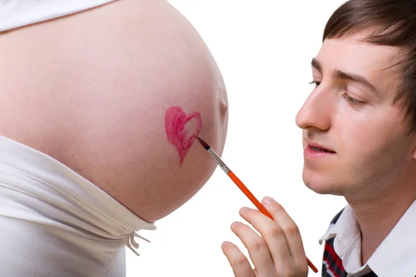 愛と待っています 彼の妻の妊娠中の腹に赤いハートを描くことにする若いハンサムな父親 — ストック写真