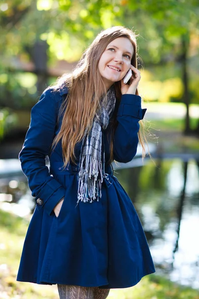 有魅力的年轻女人户外在移动电话上谈了美丽秋季的一天 — 图库照片