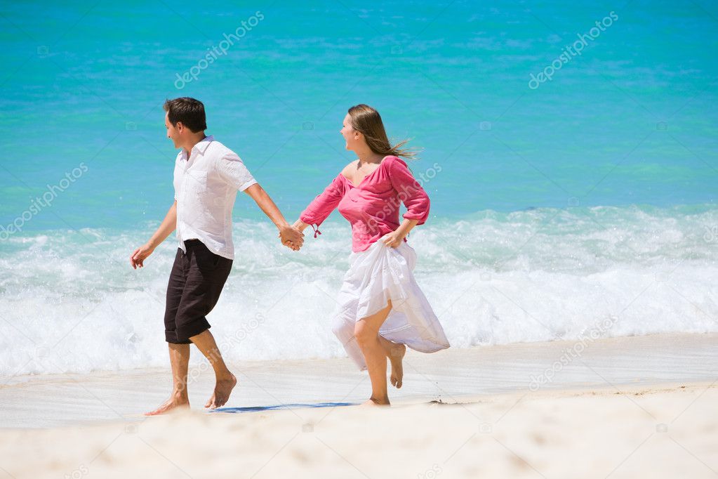 Romantic couple walking along white sand tropical beach