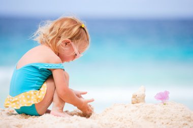 Beyaz kumsalda oynayan sevimli küçük kız.