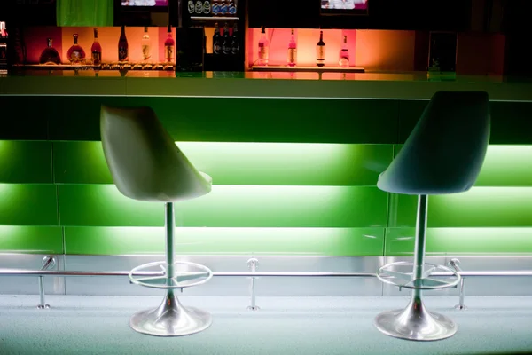 Sillas en fila en bar con botellas con luces verdes —  Fotos de Stock