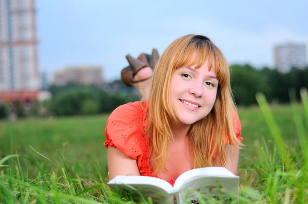 年轻微笑的女人躺在草地上，书 — 图库照片