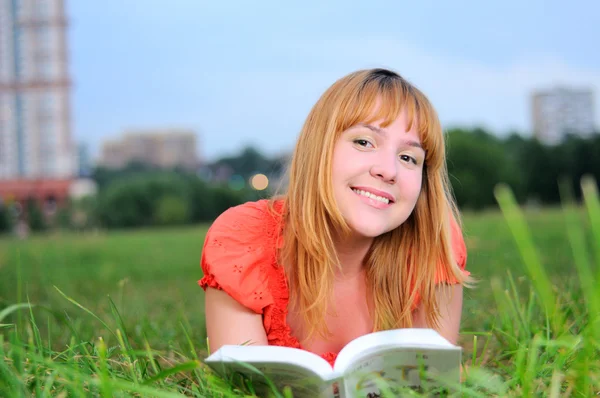 Mladá usměvavá žena ležící na louce s knihou — Stock fotografie