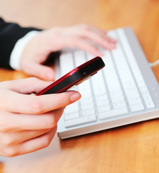 Female hands typing on a keyboard and holding mobile phone — Stock Photo, Image