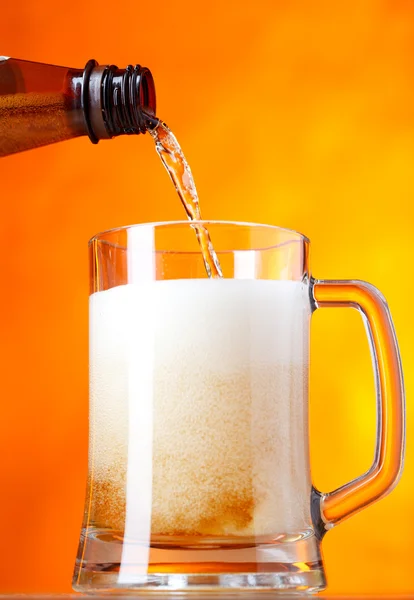 Pouring beer over orange background — Stock Photo, Image