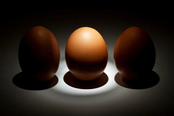 Светлое яйцо между двумя яйцами в темноте — стоковое фото