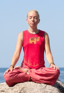 güzel bir kız bir kaya deniz üzerinde yoga egzersizleri yapıyor