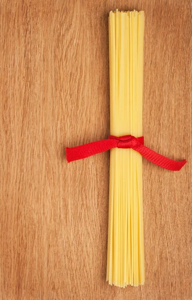 Bunch of spaghetti tied up with a red ribbon on a wooden backgro — Stock Photo, Image