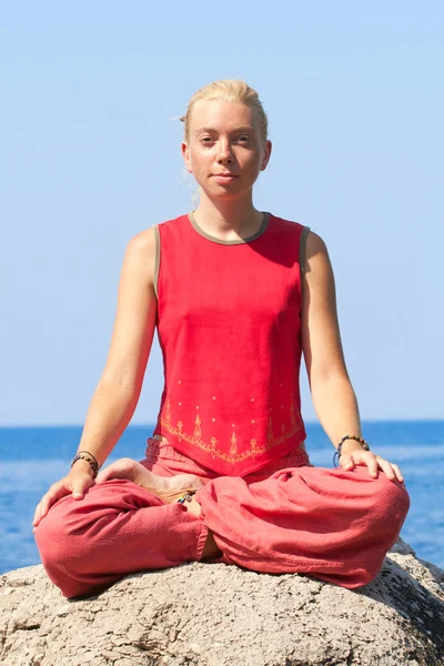Schönes Mädchen macht Yoga-Übungen auf einem Felsen in der Nähe des Meeres Stockbild