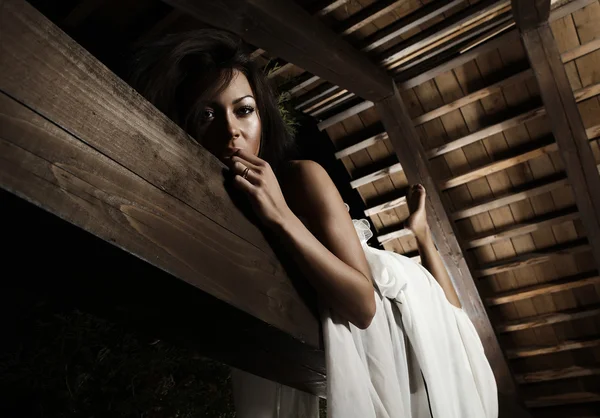 Atractiva chica bronceada en vestido blanco posa en una viga de madera . —  Fotos de Stock