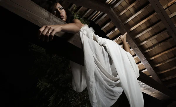 Attraktives, sonnengebräuntes Mädchen im weißen Kleid posiert auf einem Holzbalken. — Stockfoto