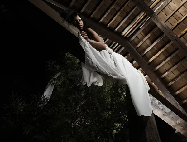 Aantrekkelijke suntanned meisje in witte jurk met zich meebrengt op een houten balk. — Stockfoto
