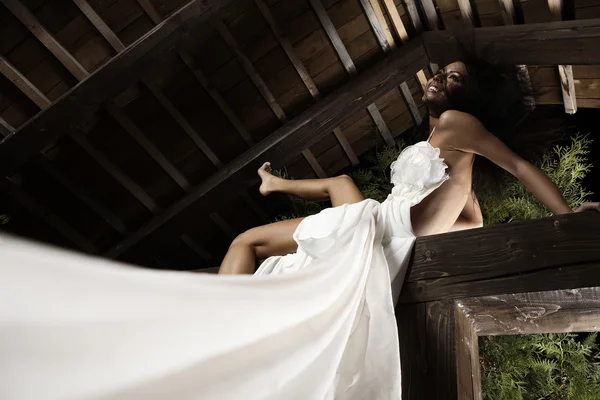 Attraktiv solbrun jente i hvit kjole stiller seg på en trebjelke . – stockfoto