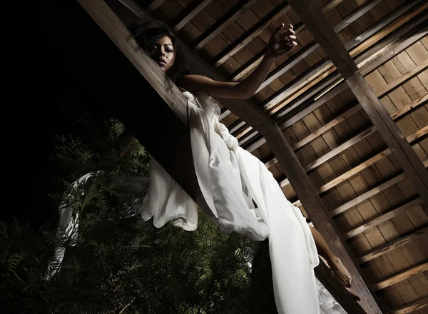 Attractive suntanned girl in white dress poses on a wooden beam. — Stock Photo, Image