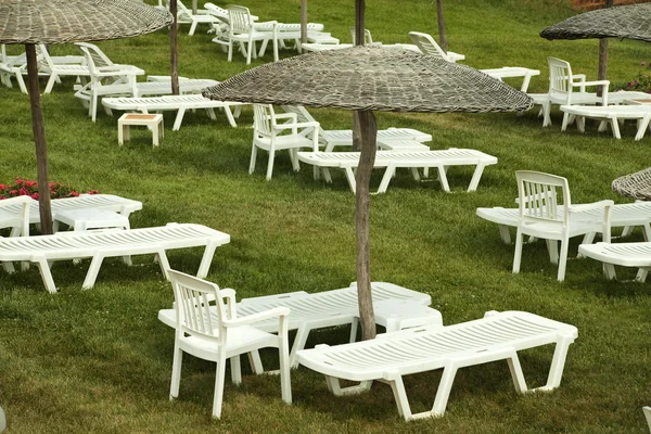 Sunbeds and umbrellas on grass in the hotel area — Stock Photo, Image