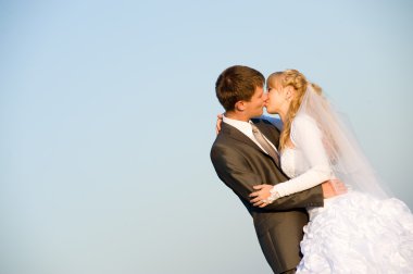 Kissing wedding pair isolated on blue sky. may be use like background for wedding cards and posters clipart