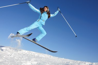 Carefree young woman in ski suit jumping, may be use for winter sports cards and posters clipart