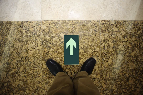 茶色の床と男の黒脚に緑色の矢印 — ストック写真