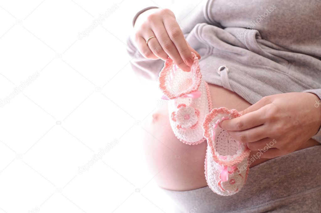 Belly of expectant mother with pink baby's bootee isolated on white