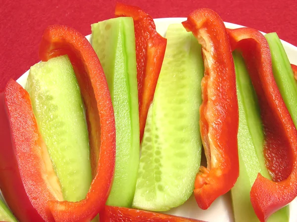 Slitted red pepper and cucumber on a white plate and placemat — Stock Photo, Image